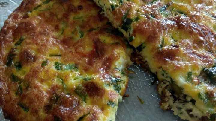 Eine goldbraune Gem&uuml;se-Frittata mit Spargel und B&auml;rlauch liegt auf einem gl&auml;sernen Teller, teilweise angeschnitten.