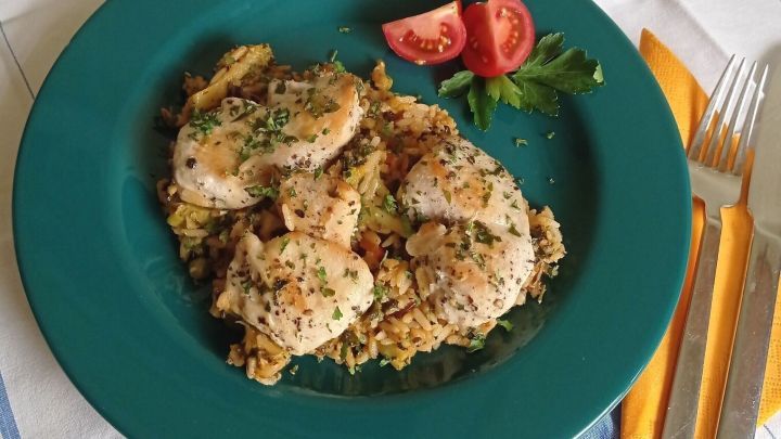 Eine bunte Wildreis-Gem&uuml;sepfanne mit H&auml;hnchenbrust liegt auf einem gr&uuml;nen Teller, umgeben von Tomaten und Petersilie.