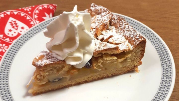 Eine Apfeltorte auf einem wei&szlig;en Teller, garniert mit Sahne, steht auf einem Holztisch neben einem festlichen Serviette.