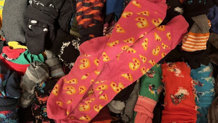 Bunte Socken sind &uuml;bereinander gestapelt, w&auml;hrend ein paar mit K&auml;se-Muster hervorstechen und die Umgebung lebhaft gestalten.