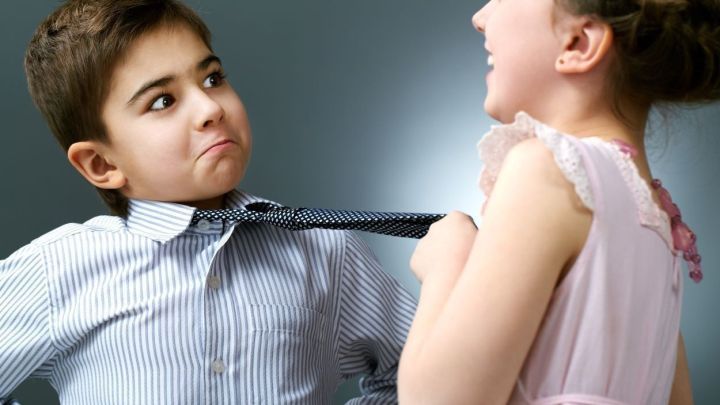 Ein Junge mit Krawatte schaut &uuml;berrascht, w&auml;hrend ein M&auml;dchen spielerisch an seiner Krawatte zieht.