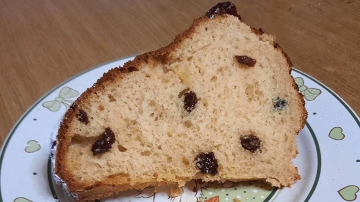 Ein Gugelhupf aus Hefeteig liegt auf einem dekorierten Teller, umgeben von einer Holzoberfl&auml;che.