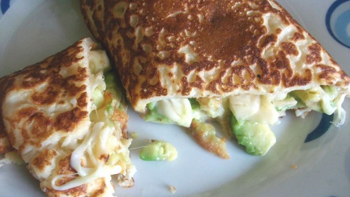 Ein Pfannkuchen mit Avocado-Bananen-K&auml;se-F&uuml;llung liegt auf einem bunten Teller und ist teilweise aufgeschnitten.