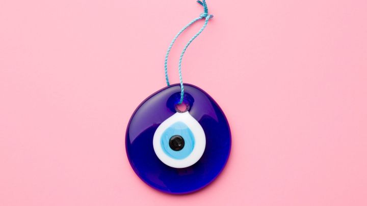 Ein blauer Gl&uuml;cksbringer h&auml;ngt an einem Faden auf einem rosa Hintergrund und symbolisiert Schutz und Wohlstand.