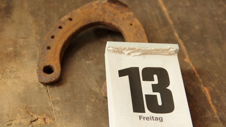 Ein rostiger Hufeisen liegt neben einem Kalenderblatt, das "13" und "Freitag" zeigt, auf einem alten Holztisch.