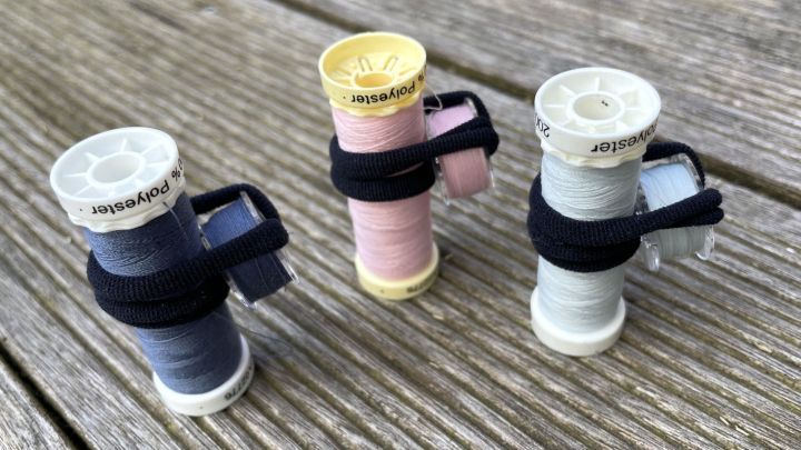 Drei Unterfadenspulen sind mit einem Band zusammengebunden und stehen auf einer Holzoberfl&auml;che.
