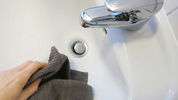 Ein gl&auml;nzendes Waschbecken wird mit einem grauen Tuch gereinigt, w&auml;hrend der Wasserhahn im Hintergrund sichtbar ist.