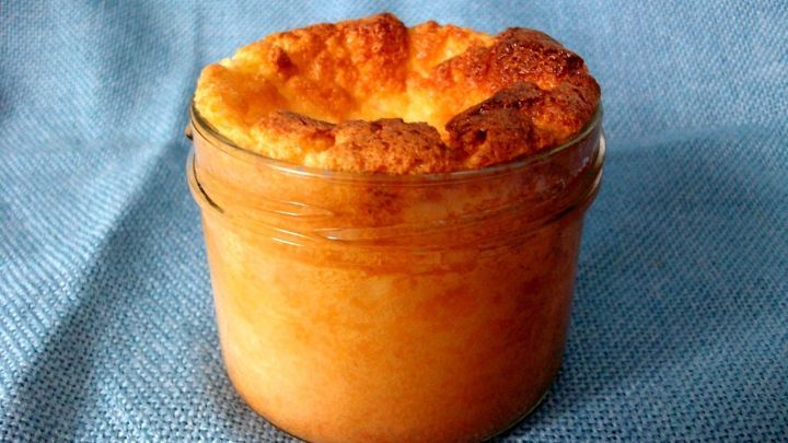 Ein Grie&szlig;kuchen-Dessert im Glas steht auf einem blauen Tuch und zeigt eine goldbraune, fluffige Oberfl&auml;che.