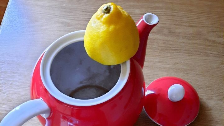 Eine rote Teekanne steht auf einem Holztisch und hat eine Zitrone auf dem Deckel platziert.