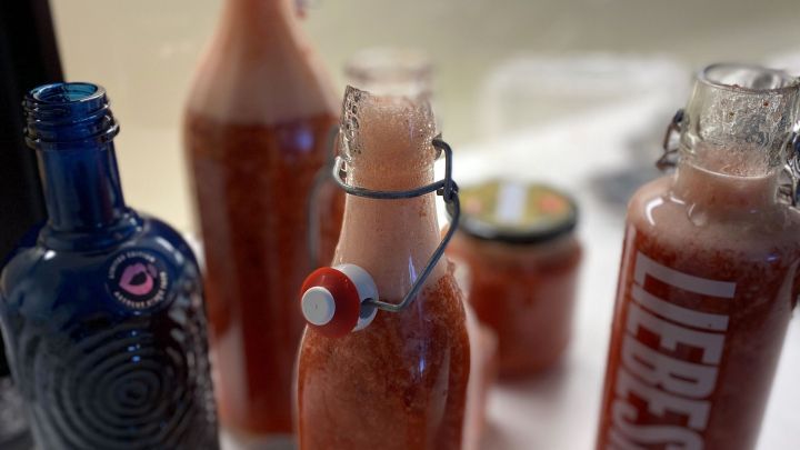 Glasflaschen mit schaumigem Erdbeer-Limes stehen auf einem Tisch, bereit f&uuml;r die Grillparty im Hintergrund.