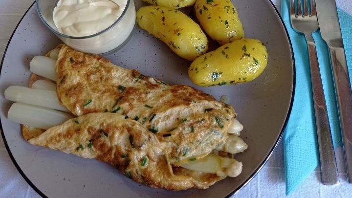 Ein Spargel-Omelette liegt auf einem Teller zusammen mit kleinen, k&ouml;stlich gew&uuml;rzten Kartoffeln und einer Portion...