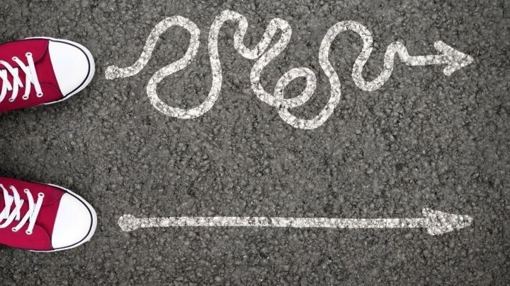 Rote Sneakers stehen auf grauem Asphalt, der mit einer gewundenen sowie einer geraden Linie markiert ist.