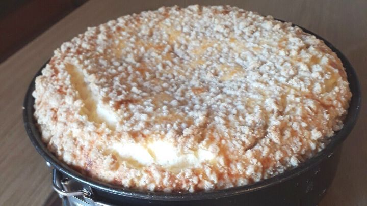 Ein K&auml;sekuchen mit Streuseln liegt auf einem Tisch. Er hat eine goldene, knusprige Oberseite und wirkt k&ouml;stlich.