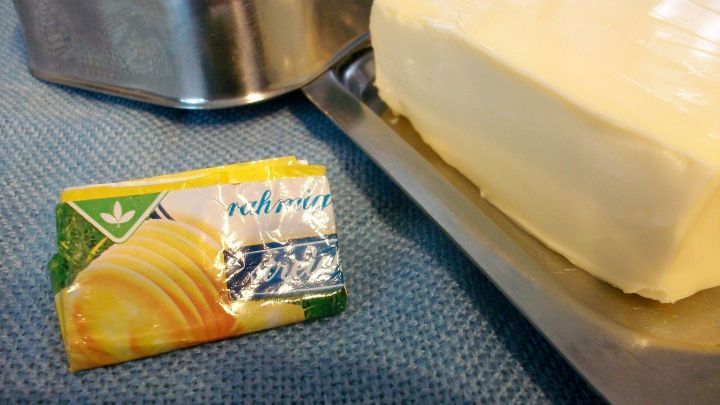 Ein St&uuml;ck Butter und das Papier von Butter liegen auf einer blauen Unterlage, bereit zum Einfetten von Blechen.