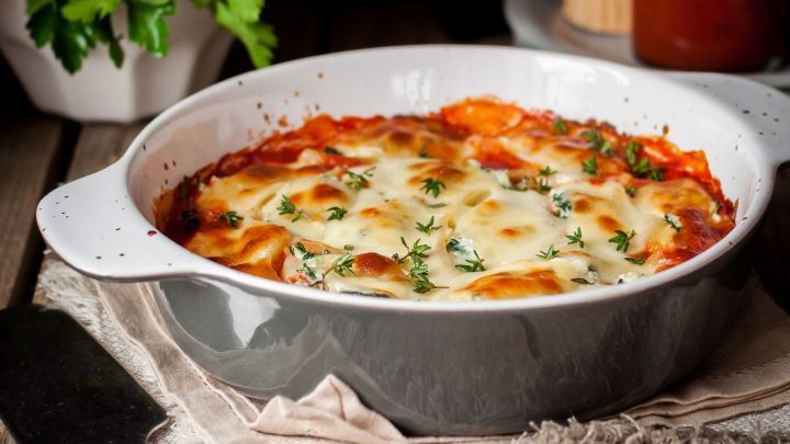 Ein leckerer Gem&uuml;seauflauf mit geschmolzenem B&uuml;ffelmozzarella wird in einer grauen Sch&uuml;ssel auf einem Holztisch pr&auml;sentiert.