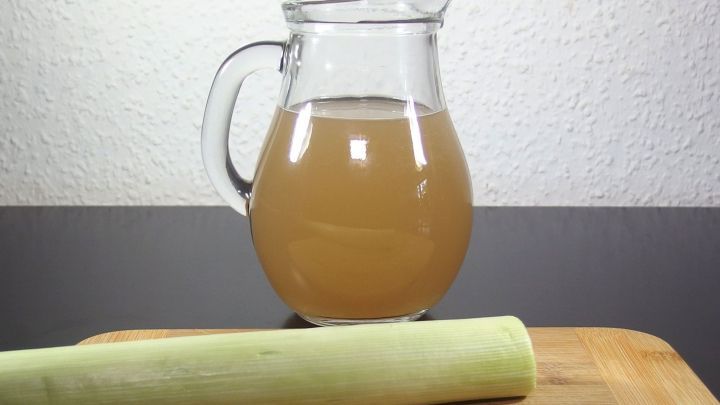 Ein transparentes Gef&auml;&szlig; mit einer braunen Fl&uuml;ssigkeit steht neben einem frischen, gr&uuml;nen Porree auf einem Holzbrett.