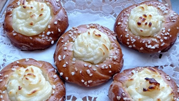 Sechs s&uuml;&szlig;e Hefeteig-Kringel mit einer cremigen F&uuml;llung und Zuckerguss auf einem dekorativen Tortenteller.