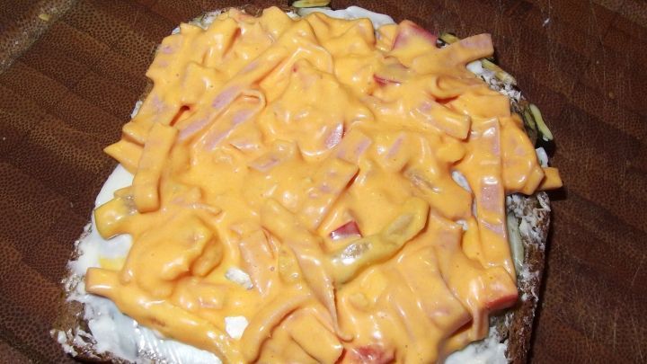 Ein belegtes Brot mit einer dicken Schicht aus gelbem K&auml;se und anderen Zutaten auf einem Holzbrett.