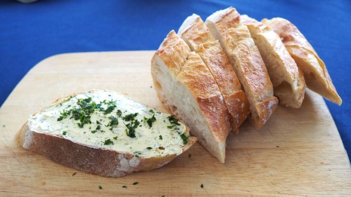 Frisches, knuspriges Brot mit veganer Kr&auml;uterbutter auf einem Holzbrett, umgeben von einem blauen Tischcloth.