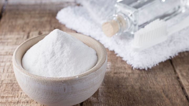 Eine Sch&uuml;ssel mit einem wei&szlig;en, pulvrigen Stoff steht auf einem Holztisch. Im Hintergrund sind ein Handtuch, ein Fl&auml;schchen und eine Zahnb&uuml;rste zu sehen.