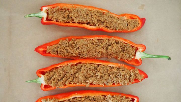 Gef&uuml;llte Paprika liegen auf einem Backpapier, gef&uuml;llt mit einer Bulgur-Mischung, bereit zum Grillen.