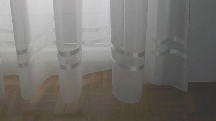 Ein transparenter Vorhang h&auml;ngt und bietet Blick auf einen hellen Raum, in dem ein Tisch und St&uuml;hle stehen.