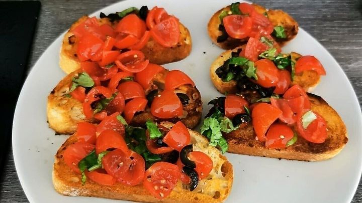Toastscheiben liegen auf einem wei&szlig;en Teller, belegt mit frischen Tomaten und Basilikum, umgeben von einer Holzoberfl&auml;che.