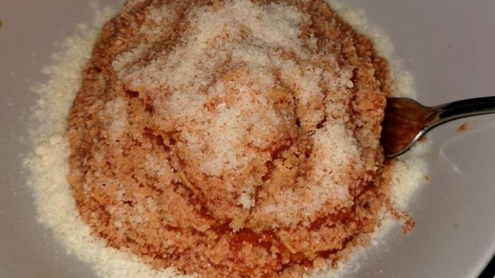 Ein Teller enth&auml;lt eine dickfl&uuml;ssige Minestrone, die mit einer Schicht von feinem K&auml;se &uuml;berzogen ist. Ein L&ouml;ffel liegt daneben.