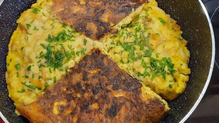 In einer Pfanne liegt ein viertel geschnittenes Pfannengericht mit Eiern und Kr&auml;utern, teilweise knusprig gebr&auml;unt.