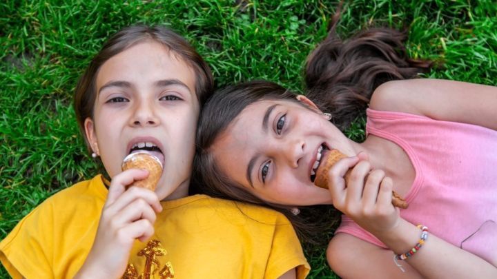 Zwei M&auml;dchen liegen auf dem Gras und essen Eis, w&auml;hrend sie l&auml;cheln und Spa&szlig; haben.