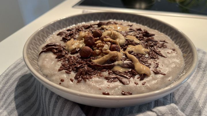 Ein Sch&uuml;ssel Milchreis ist mit Schokoladenst&uuml;ckchen, N&uuml;ssen und einer cremigen Sauce dekoriert, auf einem Tisch in einer modernen K&uuml;che.