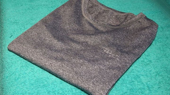 Ein ordentlich gefaltetes T-Shirt liegt auf einem gr&uuml;nen Untergrund, bereit zum Verstauen nach dem W&auml;sche falten.