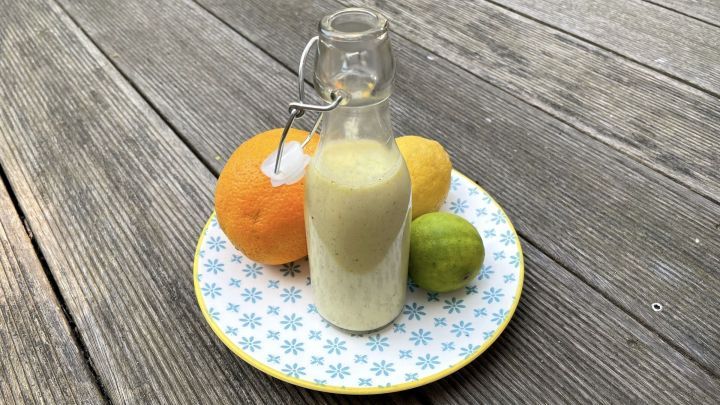 Eine Glasflasche mit Zitrus-Vinaigrette steht auf einem Teller, umgeben von Zitrusfr&uuml;chten wie Orange, Zitrone und Limette.