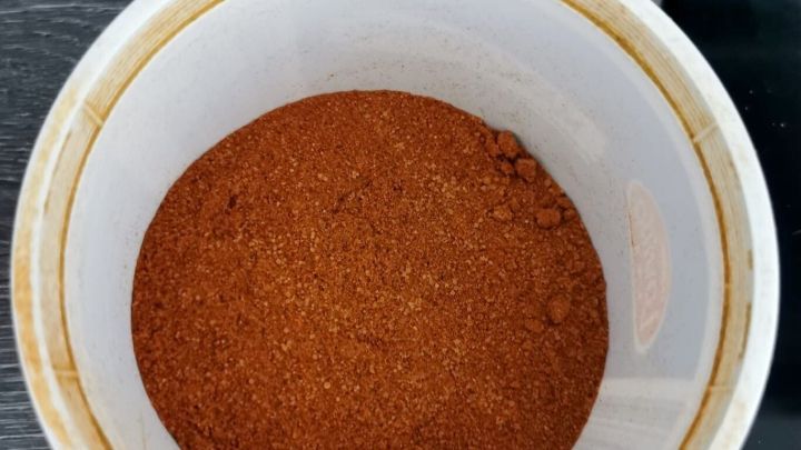 Ein wei&szlig;er Beh&auml;lter enth&auml;lt eine feine, rote Gew&uuml;rzmischung, die auf einer dunklen Arbeitsfl&auml;che steht.