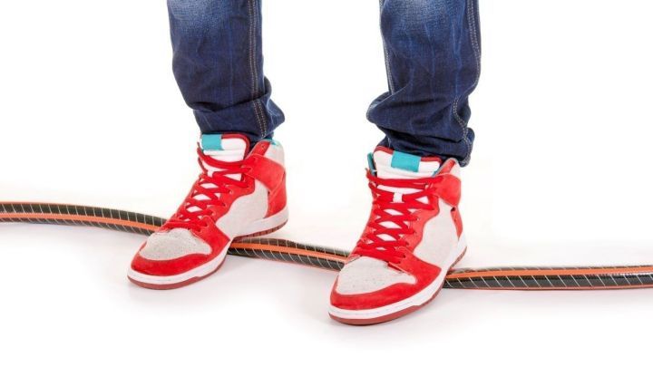 Rote Sneaker stehen auf einem Skateboard, das auf einem wei&szlig;en Hintergrund platziert ist.