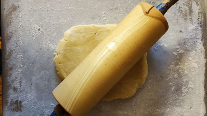 Ein Nudelholz liegt auf einem mit Mehl best&auml;ubten Backblech, w&auml;hrend es darauf wartet, den Teig auszurollen.