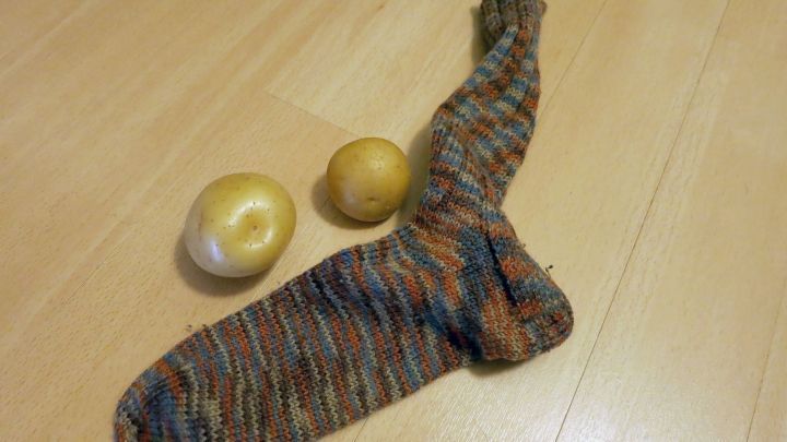 Ein gestreifter Strumpf liegt auf Holzboden, daneben zwei rohe Kartoffeln.