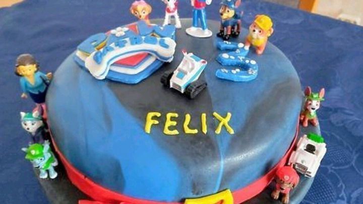 Eine bunte Geburtstagstorte mit Paw Patrol Figuren und dem Namen &bdquo;FELIX&ldquo; steht auf einem blauen Tisch.
