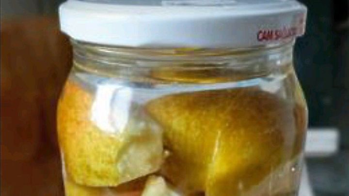 Ein Glas mit Apfelspalten, die in klarem Wasser eingeweicht sind, steht auf einem Holzuntergrund und fermentiert.