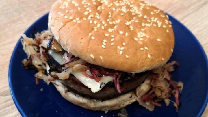 Ein Dosenwurstburger liegt auf einem blauen Teller und enth&auml;lt Wurst, K&auml;se und Kraut zwischen zwei Br&ouml;tchenh&auml;lften.
