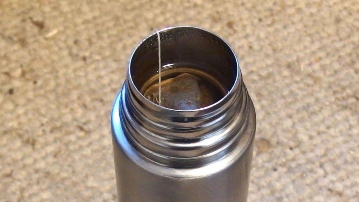 Thermoskanne mit Hagebuttentee zeigt einen Teebeutel im Inneren, auf einem strukturierten Untergrund stehend.