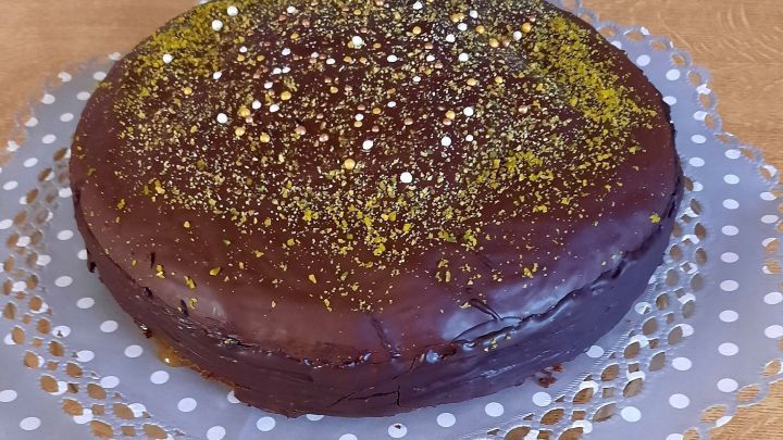 Eine Schokotorte mit Pistazien steht auf einer perforierten Serviette aus Papier, dekoriert mit bunten Streuseln.