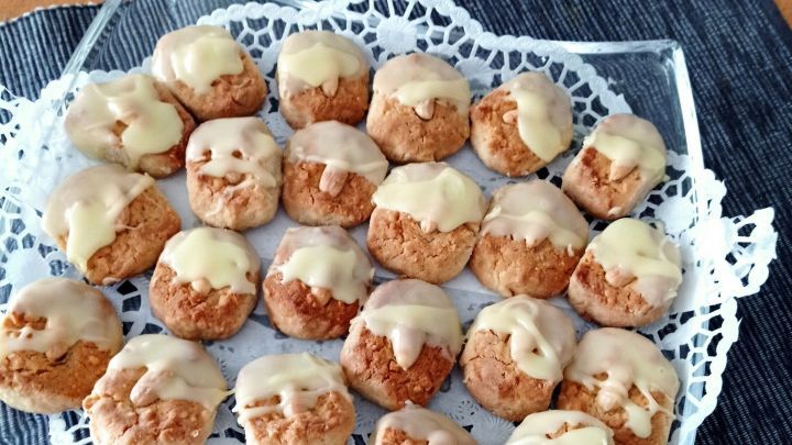 Mandelkekse auf einem Glasplatte, dekoriert mit zartem Zuckerguss, liegen auf einer wei&szlig;en Spitzenunterlage.