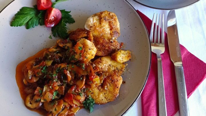 Eine appetitliche H&auml;hnchenpfanne mit w&uuml;rzigem Gem&uuml;se und Kartoffeln wird auf einem Tisch serviert, garniert mit Petersilie.