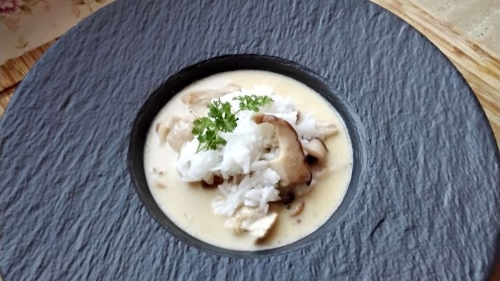 Zarte Putenbrust in einer cremigen Sauce, serviert mit frischen Steinpilzen und Reis auf einem schwarzen Teller.