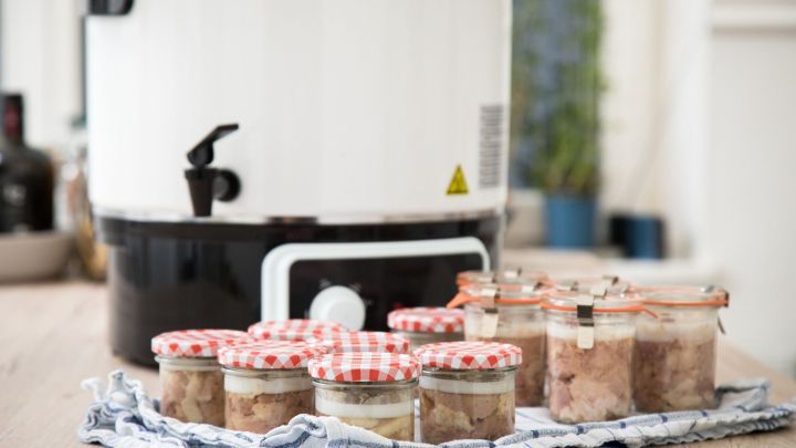 Gl&auml;ser mit aufgetautem Fleisch stehen auf einem Tuch neben einem Einmachger&auml;t in einer modernen K&uuml;che.