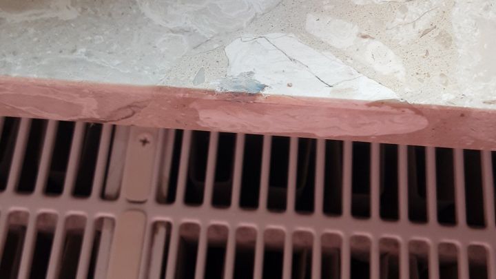 Auf der Marmorfensterbank sind Reparatur-Spachtelmasse und Ritzen sichtbar; darunter befindet sich ein Heizk&ouml;rper.