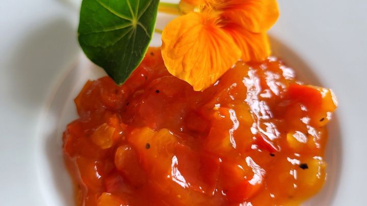 S&uuml;&szlig;e Paprikamarmelade in einem wei&szlig;en Sch&auml;lchen, garniert mit einer orangefarbenen Bl&uuml;te und einem gr&uuml;nen Blatt.