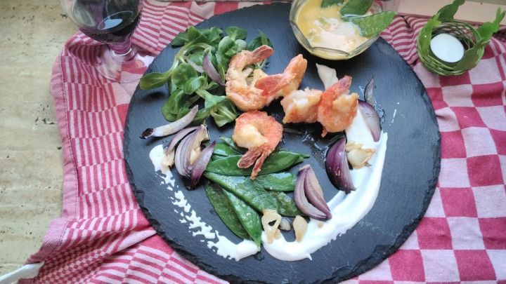 Schwarze Tiger Garnelen liegen kunstvoll auf einem schwarzen Stein, umgeben von Gem&uuml;se und einer Eierlik&ouml;r-Velout&eacute;-So&szlig;e.