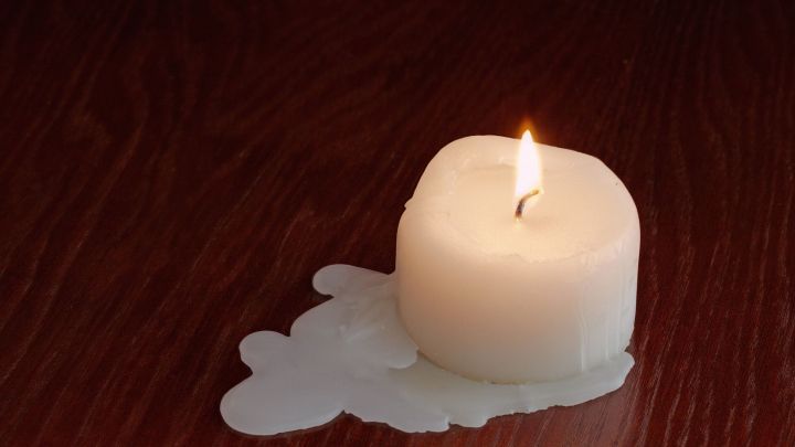 Eine brennende Kerze steht auf einem Holzuntergrund, das Wachs tropft und breitet sich unordentlich aus.